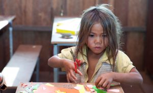 A UWS student in Cambodia enjoys colouring and cutting out shapes.